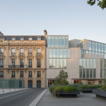 Façade d'un bâtiment historique rénové intégrant des éléments modernes en verre et acier, avec des espaces verts et éclairage naturel doux