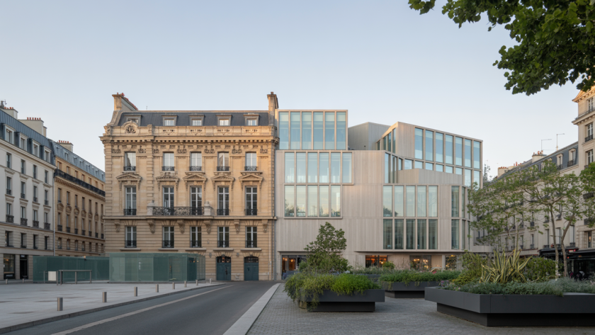 Façade d'un bâtiment historique rénové intégrant des éléments modernes en verre et acier, avec des espaces verts et éclairage naturel doux